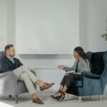 A therapist and patient engaged in conversation in a modern, stylish therapy office.