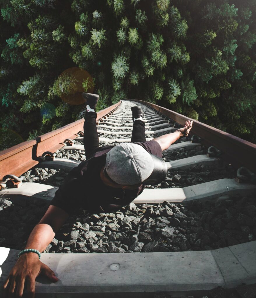 A man poses daringly over train tracks with a forest view.