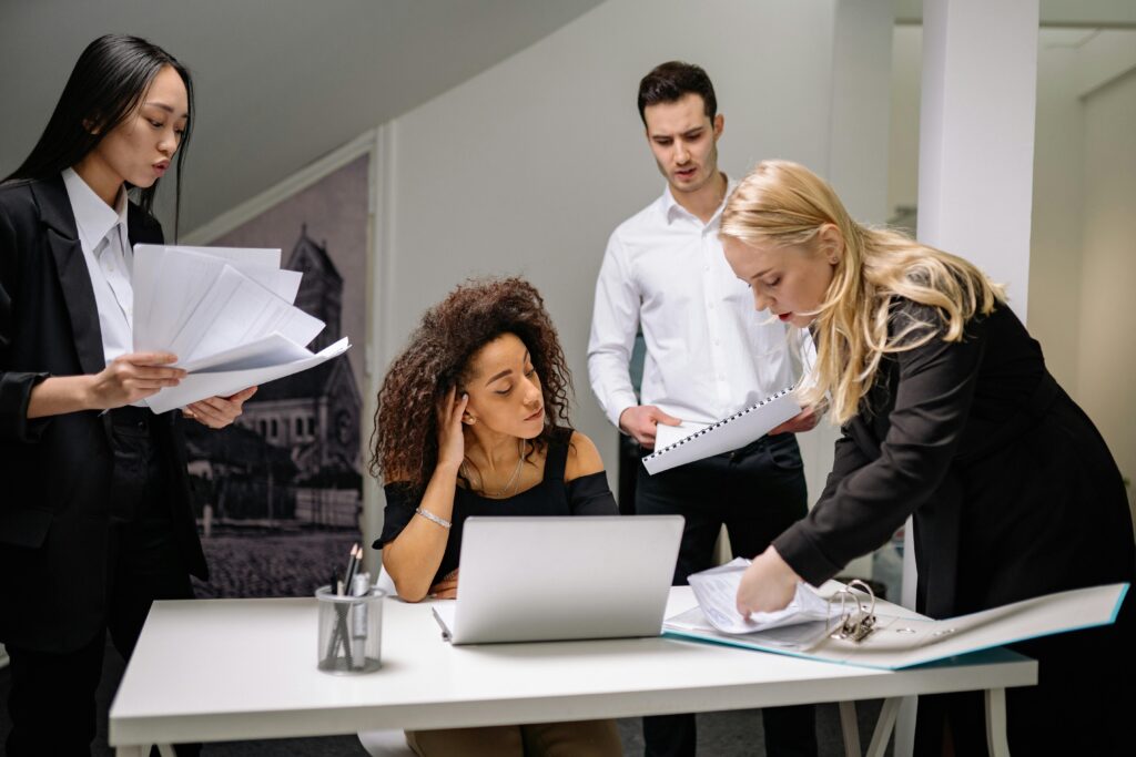 A diverse group of coworkers brainstorming over paperwork and laptops in a corporate office setting.